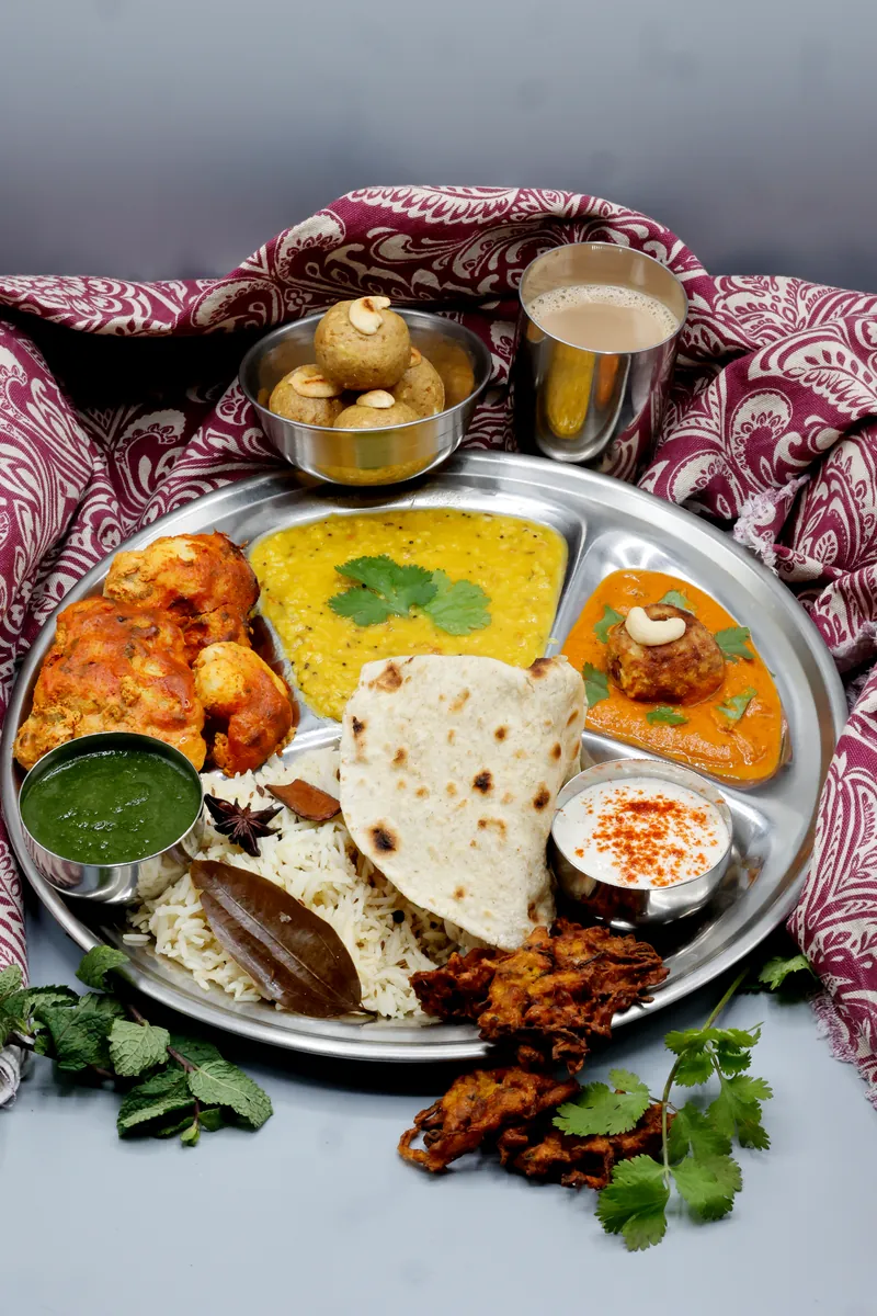 Thali indiano assortito con riso, naan, dal, pakora, chutney e dolci indiani